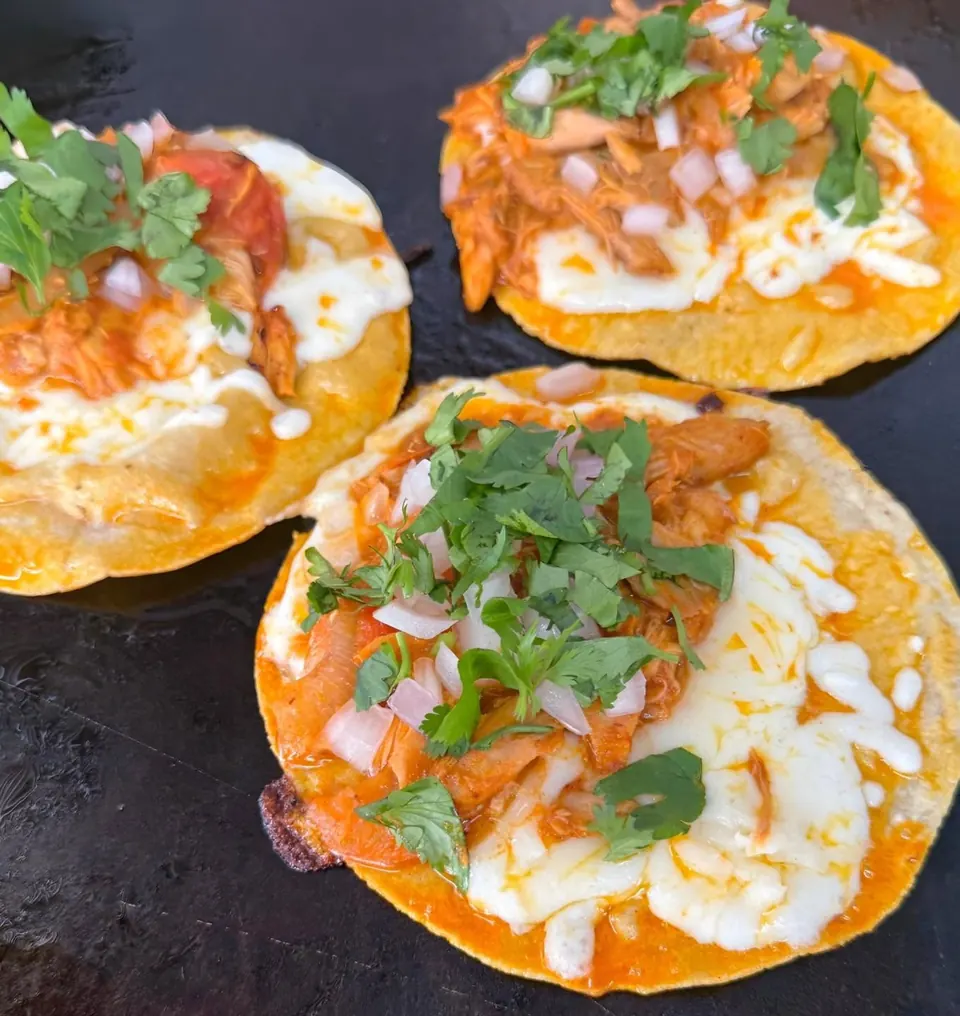 Open-faced chicken tacos with melted cheese, onions, and cilantro cooking on the griddle.
