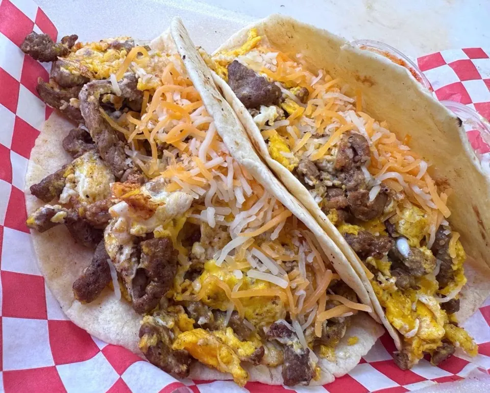 Two flour tortilla breakfast tacos loaded with meat, scrambled eggs, and shredded cheese.