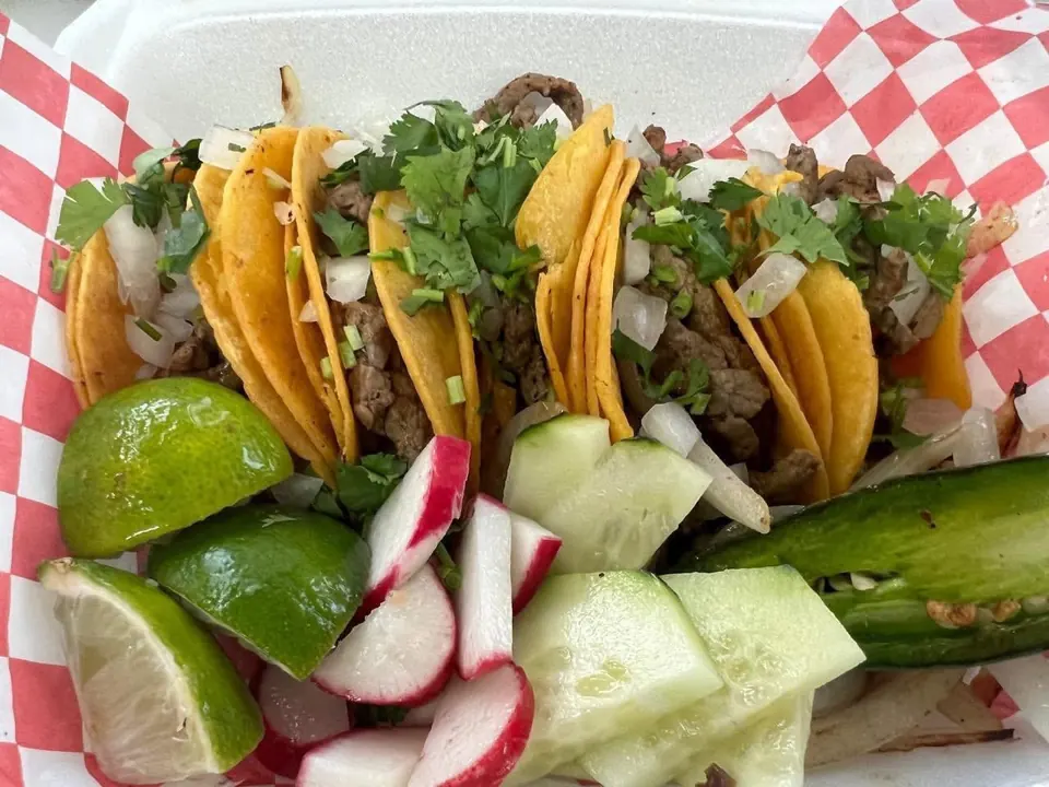 Mini street tacos with cilantro, served with lime wedges, radish, cucumber, and a grilled jalapeño.