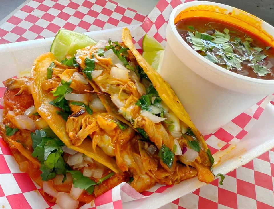 Three quesabirrias topped with onions and cilantro, served with lime and a cup of consommé.