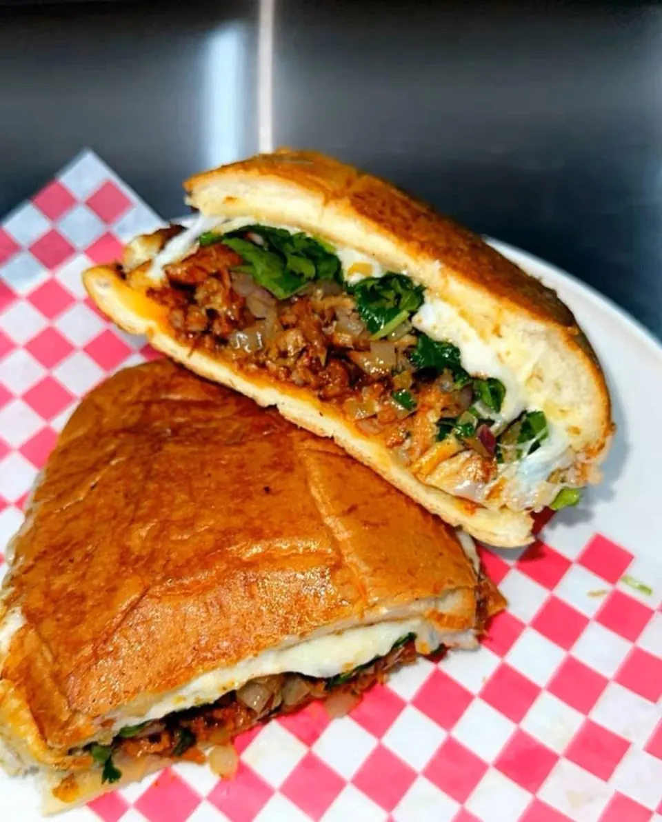 A toasted torta cut in half, filled with meat, melted cheese, and cilantro.